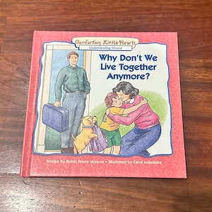 May include: A pink book titled "Comforting Little Hearts: Understanding Divorce" with the question "Why Don't We Live Together Anymore?" on the cover. The cover features an illustration of a family with a father, mother, and child. The father is holding a suitcase and walking away from the mother and child who are hugging.