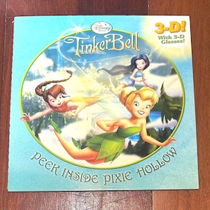 Puede incluir: Portada de libro infantil "Tinker Bell" con ilustraciones de hadas. El título es "Tinker Bell" con el texto "3-D! With 3-D Glasses!" y "PEEK INSIDE PIXIE HOLLOW". La imagen presenta un fondo azul y verde con hadas.
