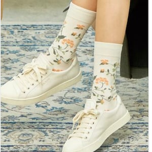 May include: A pair of white canvas sneakers with floral patterned socks. The socks have a white background with orange and green floral designs.