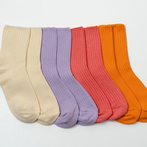 May include: Five pairs of ribbed socks in different colors: cream, lavender, coral, and orange. The socks are arranged in a row, with the toes facing the viewer.