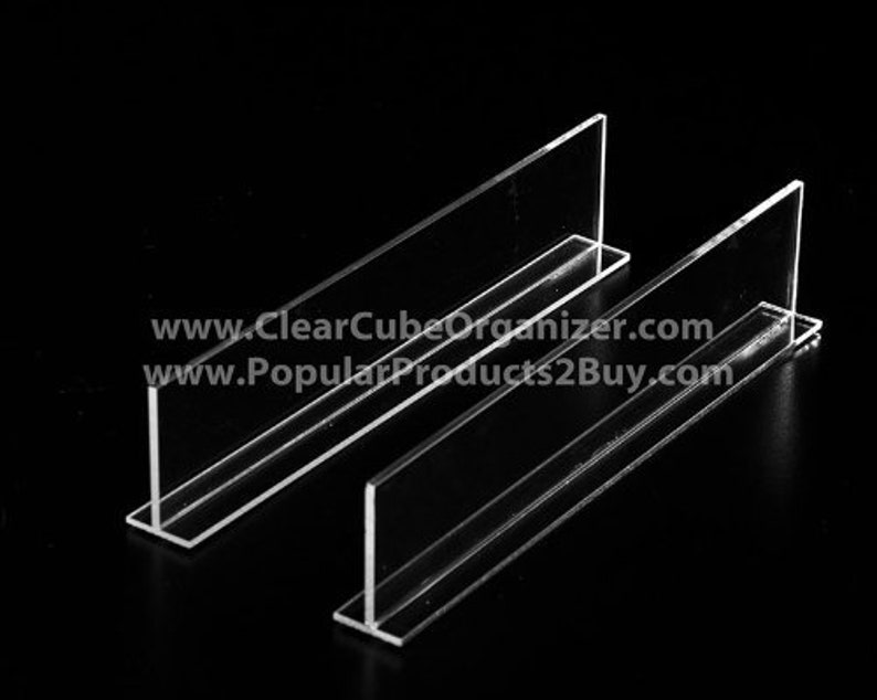 May include: Two clear acrylic shelf dividers, designed to create separate compartments within a shelf. The dividers are shaped like an upside-down 'T' and are made of sturdy, transparent acrylic.
