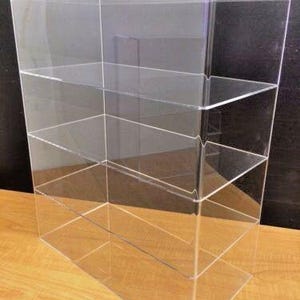 May include: Clear acrylic display case with three shelves. The case is rectangular and has a modern design.