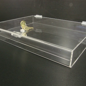 May include: A clear acrylic display case with a lock and key. The case is empty and has a rectangular shape.