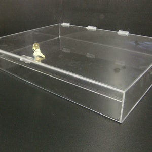 May include: A clear acrylic display case with a lock and key. The case is rectangular and has a hinged lid.