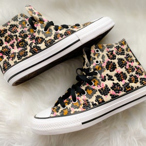 May include: A pair of high-top sneakers with a leopard print design and pink and black rhinestones. The sneakers have white soles and black laces.