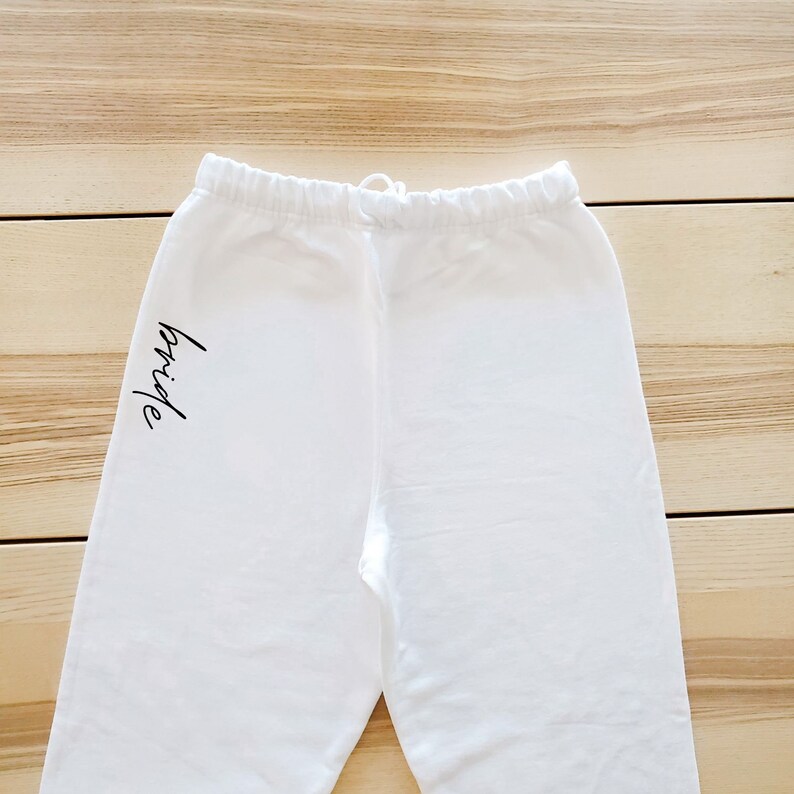May include: White sweatpants with the word "bride" written in black on the left leg.