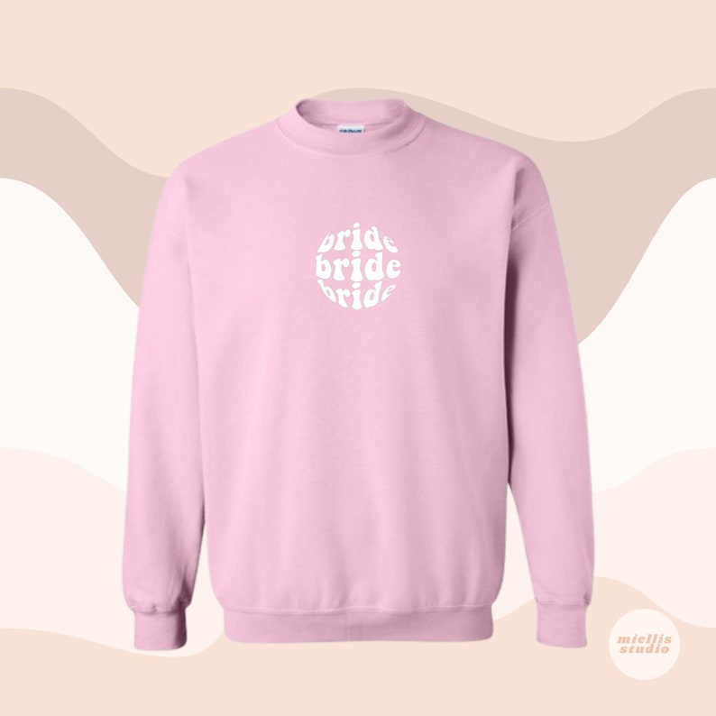 May include: A pink sweatshirt with the word "bride" written three times in a circle in a retro font.