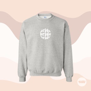 May include: A gray sweatshirt with a white circle design that says "bride" three times in a retro font.