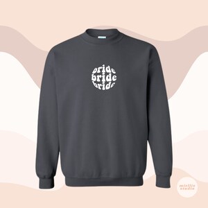 May include: Dark gray sweatshirt with a white circle graphic that says "bride" three times in a retro font.
