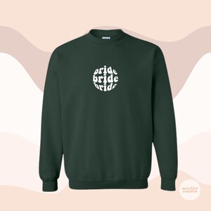 May include: A dark green sweatshirt with a white circle graphic that says "bride bride bride" in a retro font.