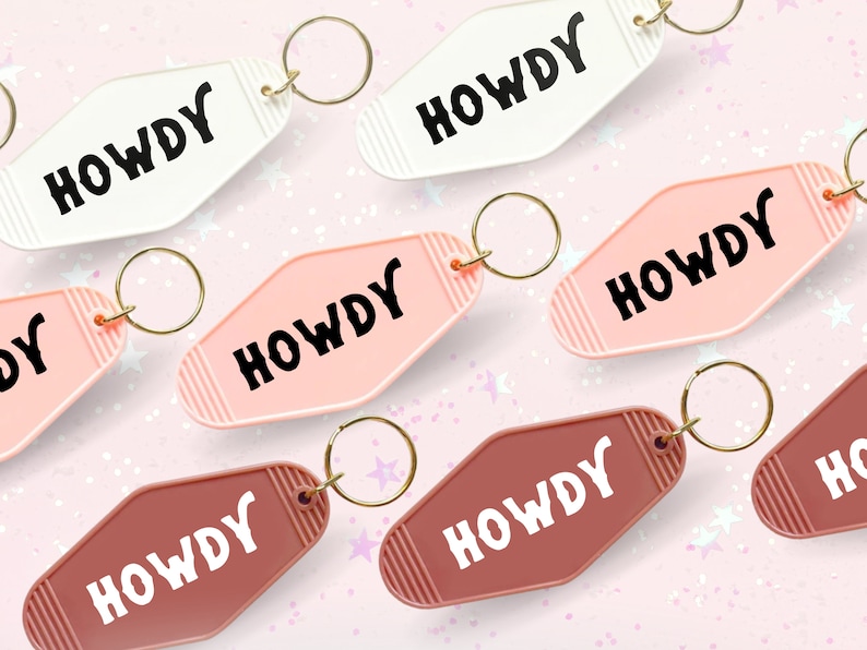 May include: A set of six keychains with the word "HOWDY" in a retro font. The keychains are in three colors: white, pink, and brown. Each keychain has a gold metal ring.