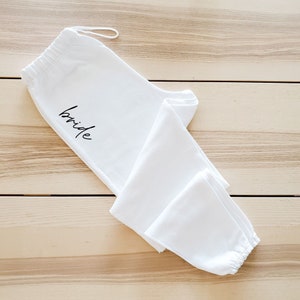 May include: White sweatpants with the word "bride" embroidered on the left leg.