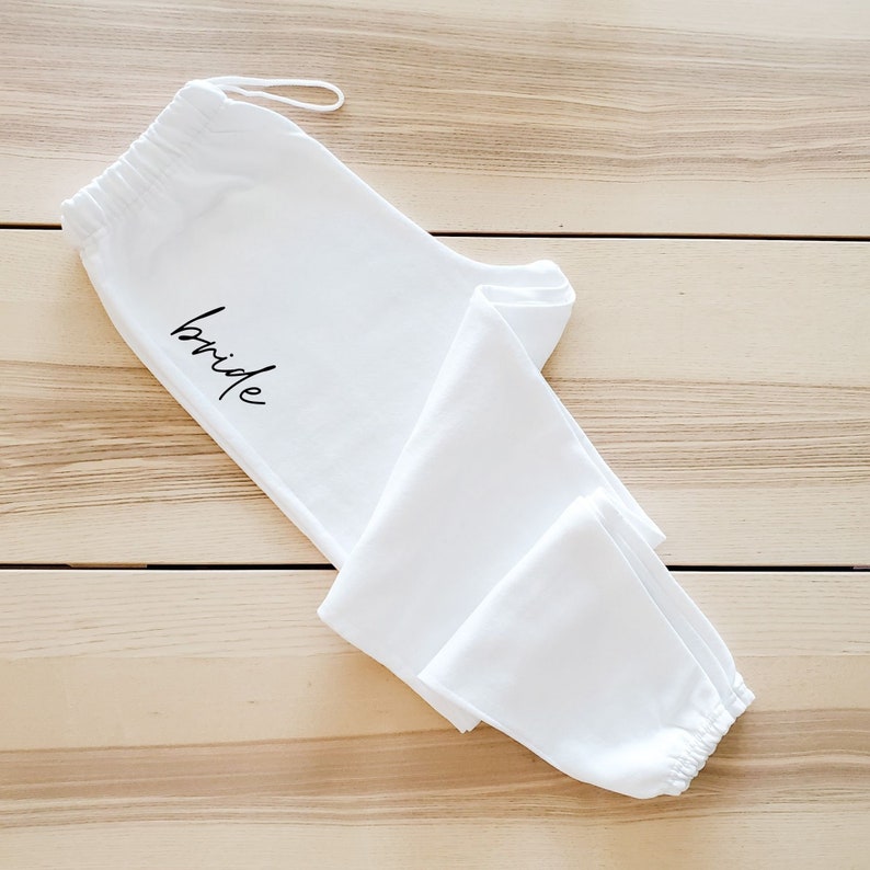 May include: White sweatpants with the word "bride" embroidered on the left leg.