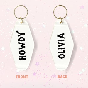 May include: White motel key chain with a gold ring. The front side says "HOWDY" in black lettering. The back side says "OLIVIA" in black lettering.