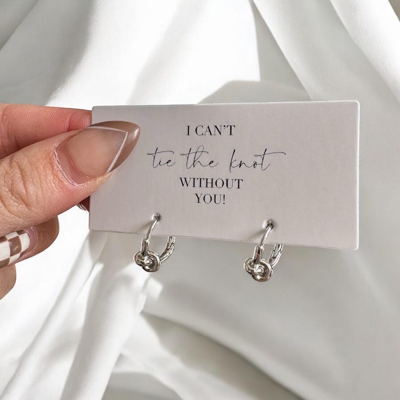 May include: A white card with the text "I can't tie the knot without you!" and two silver knot hoop earrings.