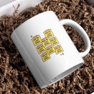 May include: White ceramic mug with the text "PER MY LAST EMAIL" printed on yellow sticky notes. The mug is inside a white box filled with brown paper shreds. The mug has a white handle and a simple design.