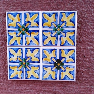 Könnte beinhalten: Vier quadratische Keramikfliesen mit blau-weißem Hintergrund und gelben und grünen Blumendesigns.