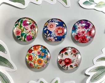 May include: Five round glass magnets with floral patterns. The magnets feature different floral designs in shades of pink, red, blue, yellow, and green.
