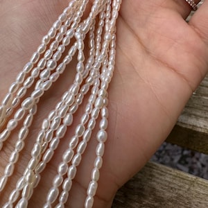 May include: A close-up view of several strands of creamy white, oval pearls. The pearls are strung together, creating a flowing, elegant appearance. The image highlights the natural lustre and subtle variations on the pearl's surface, suggesting a high-quality jewellery piece.