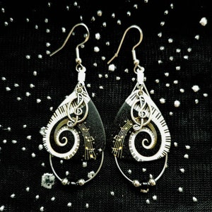 May include: A pair of black and white dangle earrings with a silver treble clef charm. The earrings feature a spiral design with gold musical notes.