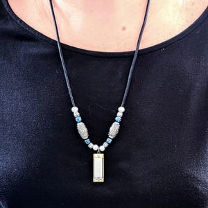 May include: A black leather necklace with silver and blue beads and a small harmonica pendant.