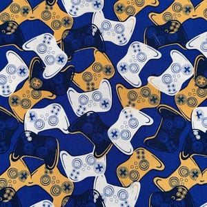 May include: A fabric pattern featuring a repeating design of video game controllers in white, navy blue, and gold against a royal blue background. The controllers have circular buttons and directional pads.