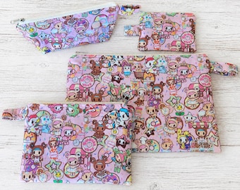 May include: A set of five pink zippered pouches with a colorful cartoon character and dessert pattern. The pouches vary in size and shape, with a long, narrow pouch and four rectangular pouches.