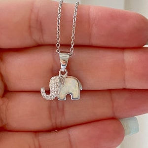 May include: A silver chain necklace with a small, white opal elephant pendant. The elephant has clear cubic zirconia stones on its head and trunk.