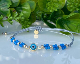 May include: A gray string bracelet with blue and gold beads and a blue evil eye charm.