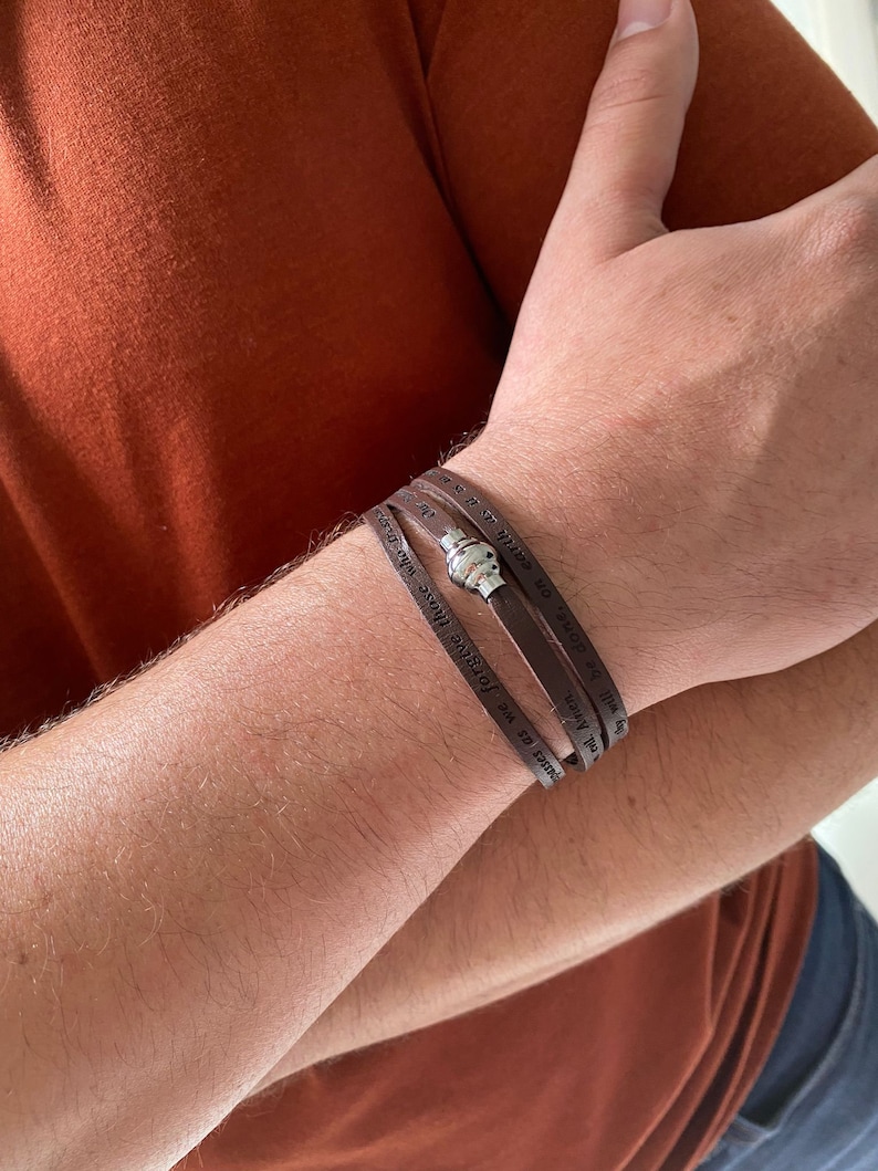May include: A brown leather bracelet with the words "In faith we forgive those who have wronged us. Amen." and "Will be done, on earth as it is in heaven." engraved on it.