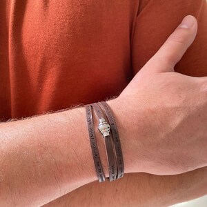 May include: A brown leather bracelet with a silver charm and the text "Forgive those who trespass against us as we forgive those who trespass against us. Amen. A will be done, on earth as it is in heaven."