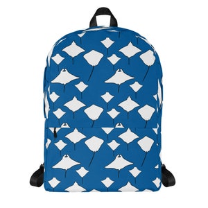 May include: A blue backpack with a repeating pattern of white manta rays. The backpack has black straps, a top handle, and a front pocket with a black zipper. The design features various sizes of the manta ray illustration.