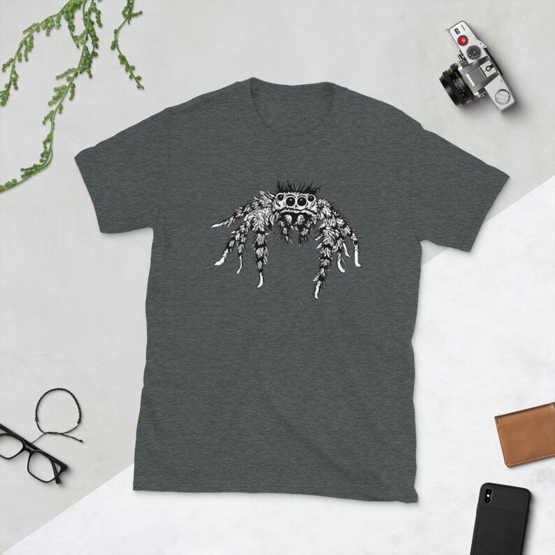 Puede incluir: Camiseta gris oscuro con una ilustraci&oacute;n detallada en blanco y negro de una ara&ntilde;a saltarina. El dise&ntilde;o de la ara&ntilde;a est&aacute; centrado en la camiseta, mostrando patrones y texturas intrincados. La camiseta est&aacute; hecha de un material suave.