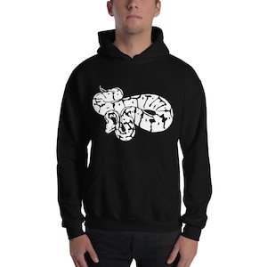 May include: Black hooded sweatshirt featuring a white graphic of a coiled snake. The snake design has a detailed pattern with black and white markings. The sweatshirt has a front pocket and a drawstring hood.