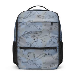 Peut inclure: Sac à dos avec un motif de requins noirs et blancs sur fond bleu clair. Il possède une poignée noire, des poches latérales en filet noir et des fermetures éclair noires. Le design présente diverses espèces de requins.