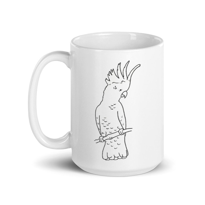 May include: White ceramic mug featuring a black and white line drawing of a cockatoo perched on a branch. The bird is depicted in a simple, illustrative style. The mug has a curved handle and a glossy finish.