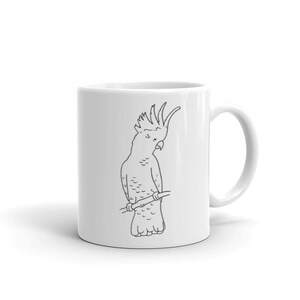 May include: White ceramic mug featuring a black line drawing of a cockatoo perched on a branch. The bird is depicted with its distinctive crest and a slightly tilted head. The mug has a curved handle and a glossy finish.