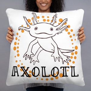 May include: White square cushion with a black and white axolotl illustration and orange accents. The word "AXOLOTL" is printed in black block letters below the axolotl design. The cushion has a soft, plush appearance.