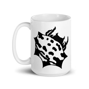 May include: White ceramic mug with a black and white shell design. The shell illustration has a spotted pattern. The mug has a curved handle and a glossy finish. Ideal for hot beverages.