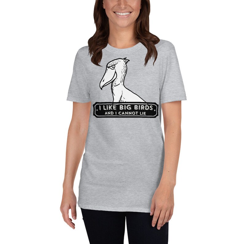 May include: A light gray t-shirt featuring a Shoebill bird illustration with the text "I LIKE BIG BIRDS, AND I CANNOT LIE" in a black and white design. The shirt is made of a soft material.