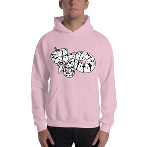 May include: A light pink hooded sweatshirt featuring a black and white snake graphic on the front. The snake is coiled and has a detailed pattern. The sweatshirt has a kangaroo pocket and a drawstring hood.