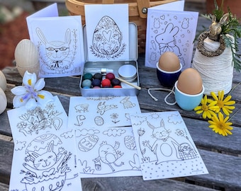 May include: A set of Easter-themed coloring pages featuring bunnies, eggs, and flowers. The set includes a small tin of paint and paintbrushes. The pages are printed on white cardstock and are ready to be colored.