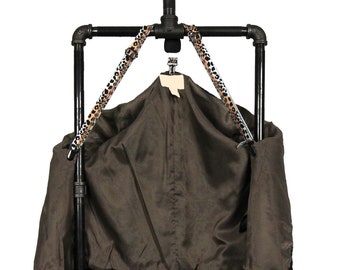 May include: A black metal garment rack with a leopard print strap hanging a brown jacket with black sleeves.
