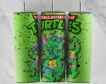 May include: Green stainless steel tumbler with a graphic of the Teenage Mutant Ninja Turtles. The turtles are in a fighting pose with their weapons. The background is green with black splatters.