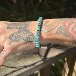 May include: A silver bracelet with a row of turquoise stones in various shades of blue and green.