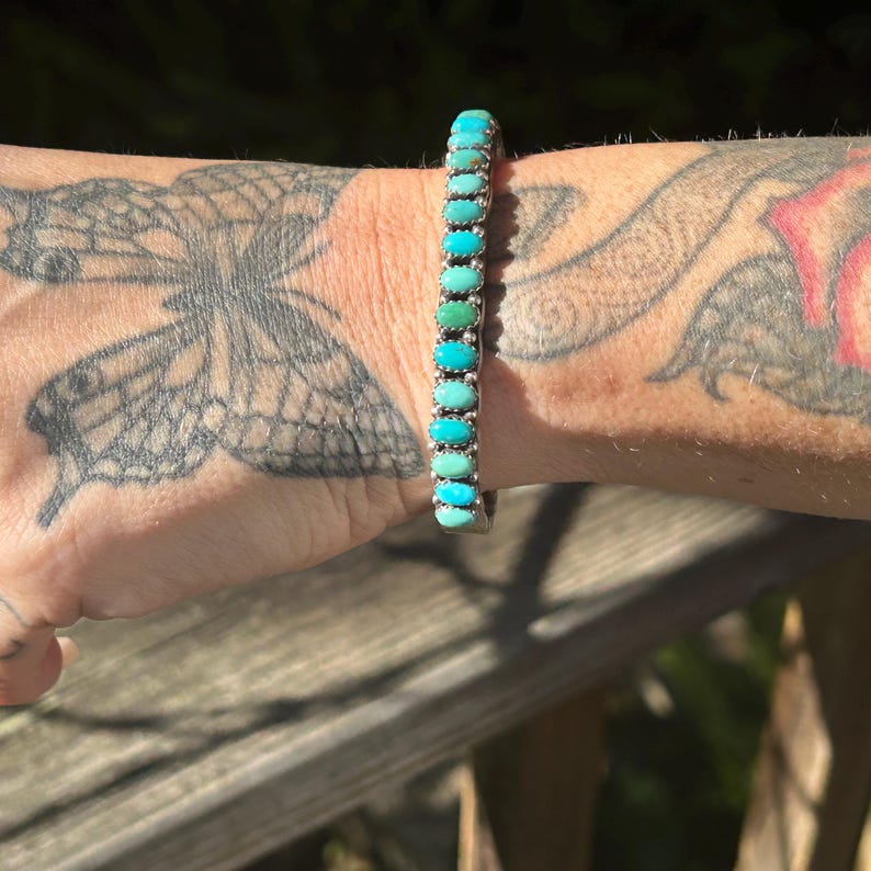 May include: A silver bracelet with a row of turquoise stones in graduated shades of blue and green.