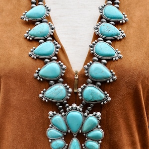 May include: A statement necklace featuring large, teardrop-shaped turquoise stones set in silver-toned metal. The necklace has a layered design with smaller turquoise accents and a beaded chain, creating a bold, eye-catching accessory.