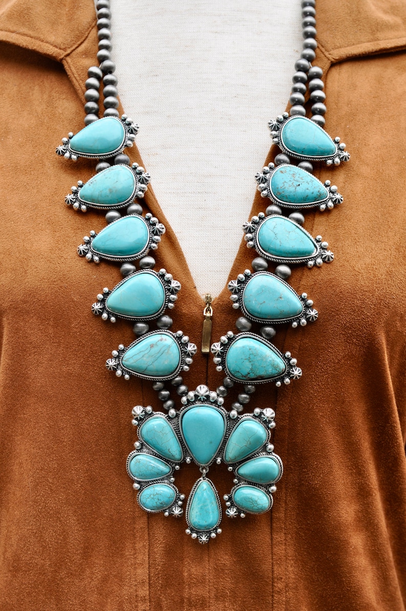 May include: A statement necklace featuring large, teardrop-shaped turquoise stones set in silver-toned metal. The necklace has a layered design with smaller turquoise accents and a beaded chain, creating a bold, eye-catching accessory.