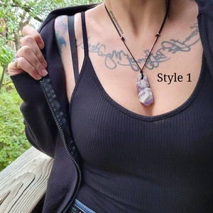 Peut inclure: Un d&eacute;bardeur noir c&ocirc;tel&eacute; avec une veste noire et un collier pendentif. Le collier pr&eacute;sente un grand pendentif en cristal rectangulaire violet et blanc sur un cordon noir. Le texte "Style 1" est visible.