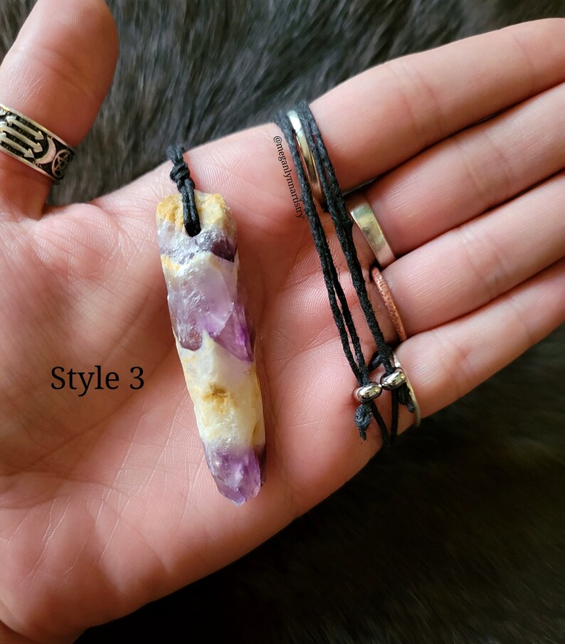 Peut inclure: Pendentif en cristal d'am&eacute;thyste brut sur un collier en cordon noir. Le cristal pr&eacute;sente des nuances de violet, de blanc et de jaune. Le collier est pr&eacute;sent&eacute; sur une main, avec des bagues aux doigts. Le texte "Style 3" est visible.
